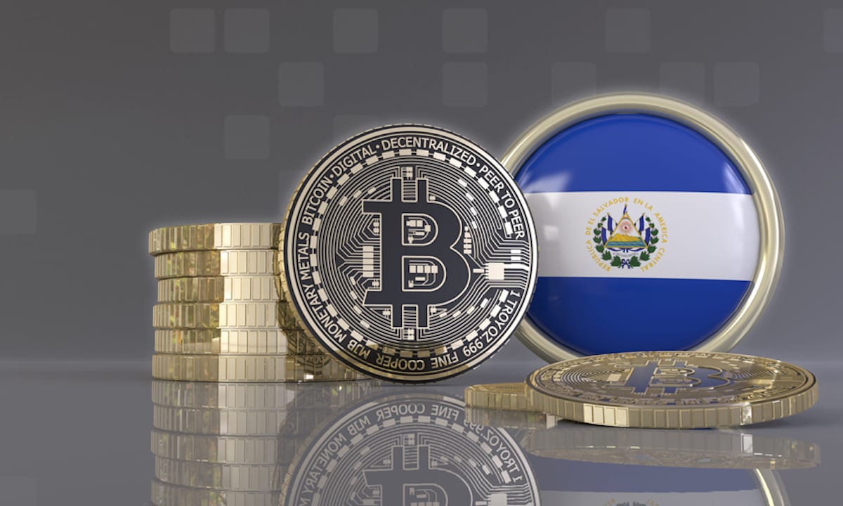 Picture of a round El Salvador flap with a silver bitcoin next to it, and a stack of coins behind the bitcoin